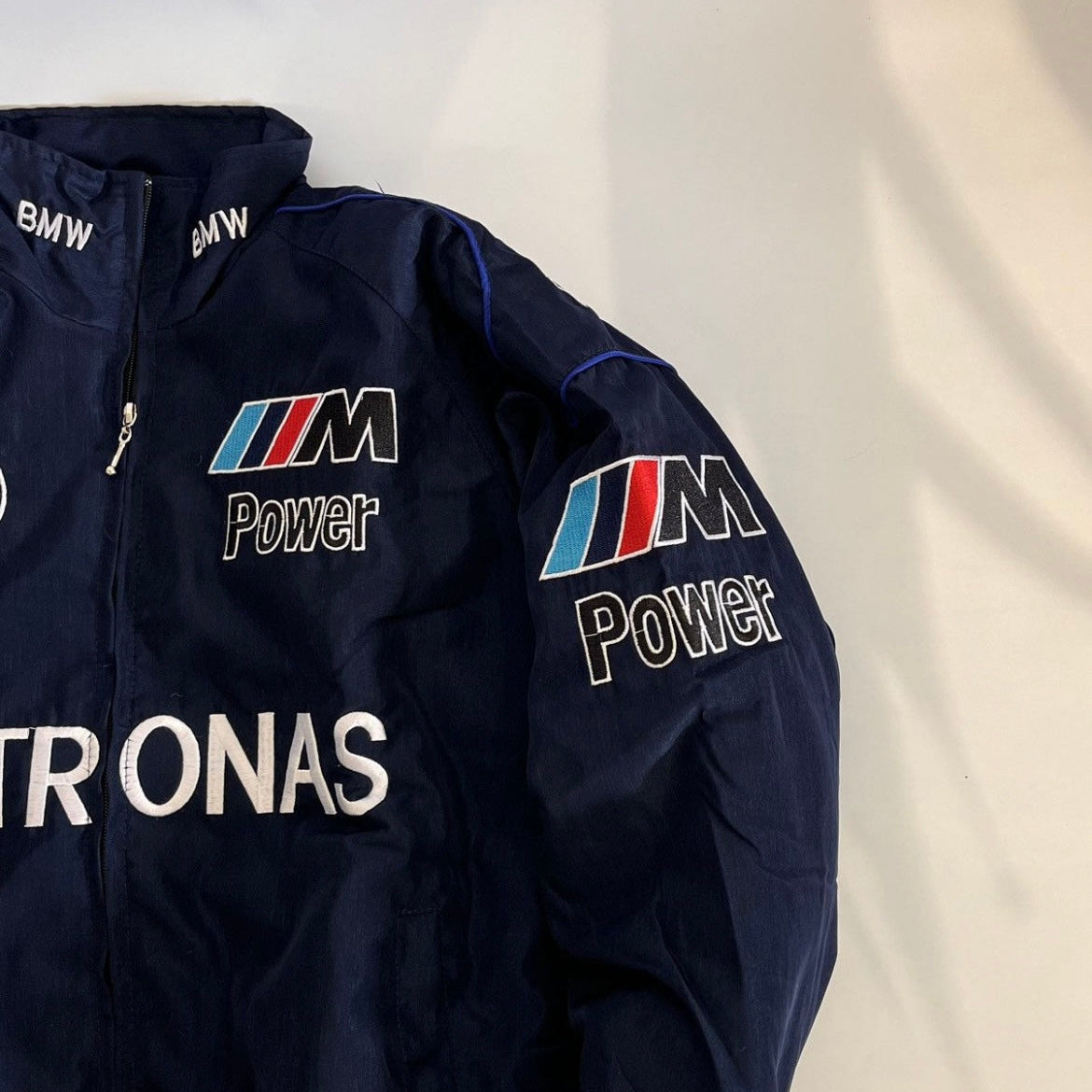 A navy blue BMW Motorsport jacket featuring the BMW M Power logo on the chest and sleeve, with 'PETRONAS' branding on the lower front, shown against a plain light background.